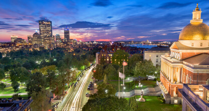 View of downtown Boston at sunset, featuring the illuminated Massachusetts State House with its golden dome and adjacent city park—a picturesque scene that even lawyers in Chicago would admire.