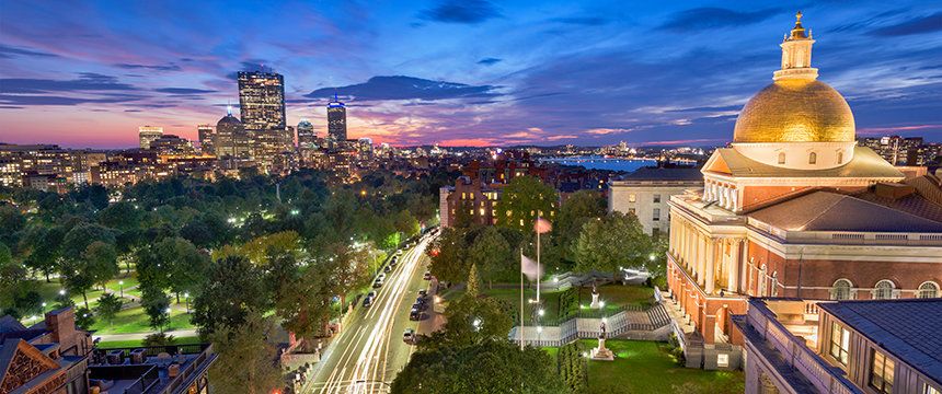 View of downtown Boston at sunset, featuring the illuminated Massachusetts State House with its golden dome and adjacent city park—a picturesque scene that even lawyers in Chicago would admire.