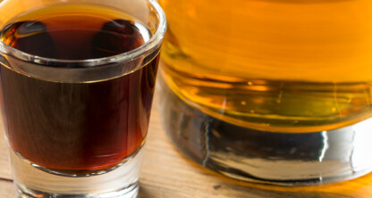 A close-up of a shot glass filled with dark liquor next to a glass of amber-colored liquor on a wooden surface, perfect for unwinding after a busy day at law offices or celebrating with fellow Chicago lawyers.