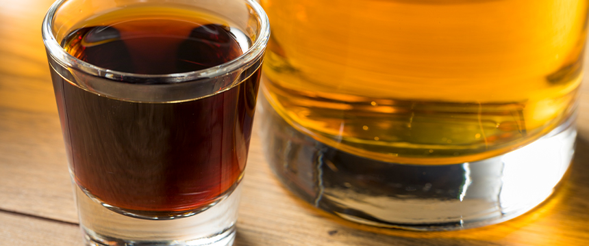A close-up of a shot glass filled with dark liquor next to a glass of amber-colored liquor on a wooden surface, perfect for unwinding after a busy day at law offices or celebrating with fellow Chicago lawyers.