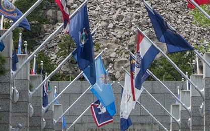 A stone memorial archway with multiple U.S. state flags displayed, flanked by trees on both sides, evokes the integrity and tradition found in a corporate law office dedicated to intellectual property law.