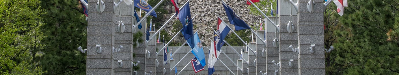 A stone memorial archway with multiple U.S. state flags displayed, flanked by trees on both sides, evokes the integrity and tradition found in a corporate law office dedicated to intellectual property law.