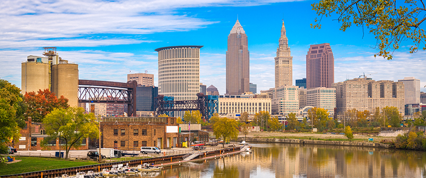 Downtown Cleveland skyline with modern and historic buildings, autumn foliage, and the Cuyahoga River in the foreground—an urban view reminiscent of a bustling corporate law office district.