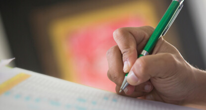 A person holds a green pen and writes on a sheet of paper with printed text and numbers, possibly preparing documents for a corporate law office or litigation support.