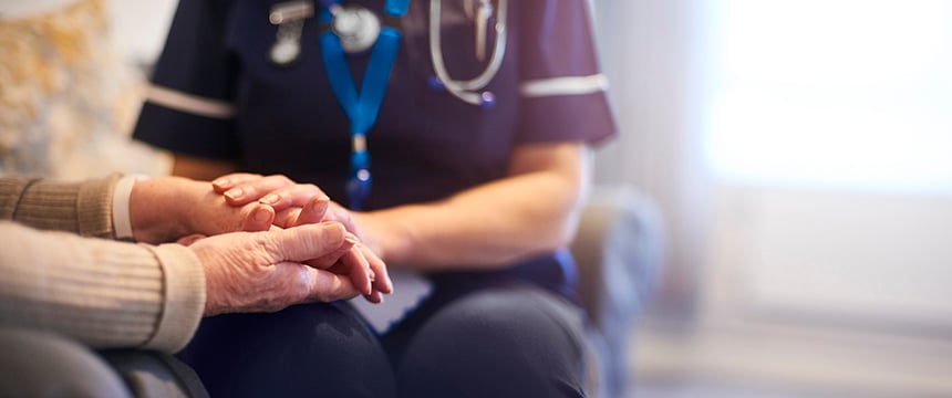 A healthcare professional in uniform holds the hands of an elderly person, providing comfort and support—much like litigation support assists clients in challenging times—in a well-lit indoor setting.