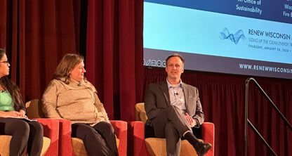 Three panelists sit on stage in armchairs at the RENEW Wisconsin Energy Summit, with a presentation screen and red curtain in the background, discussing how law offices can offer litigation support for clean energy initiatives.
