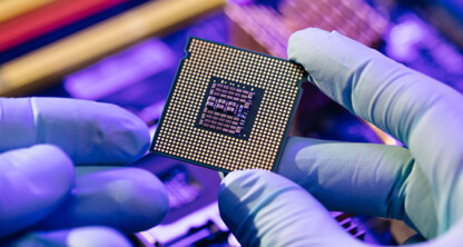 Gloved hands hold a computer processor above a blurred background of electronic components under blue and purple lighting, capturing the advanced technology often utilized by law offices for litigation support.