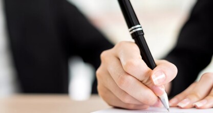 Close-up of a person holding a black pen and writing on a sheet of paper, with another person beside them in the background—capturing a moment inside one of the leading law offices in Chicago.