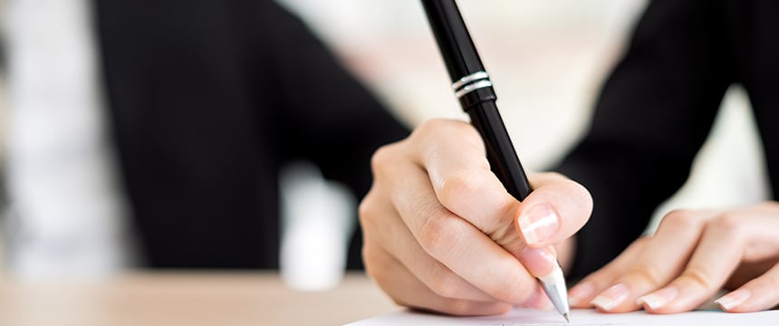 Close-up of a person holding a black pen and writing on a sheet of paper, with another person beside them in the background—capturing a moment inside one of the leading law offices in Chicago.