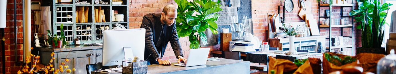 A man stands at a desk in a modern, plant-filled law office, working on a laptop and a desktop computer against an exposed brick wall background, providing litigation support for lawyers in Chicago.