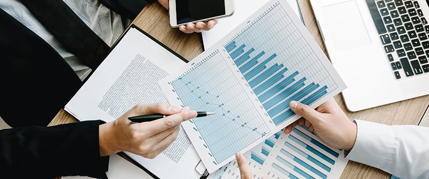 Two lawyers in Chicago review and discuss printed bar and line graphs at a desk with documents, a notebook, and a smartphone, providing litigation support for intellectual property law cases.
