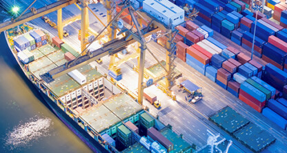 Aerial view of a busy shipping port at night with cargo containers, cranes, and a docked cargo ship by the water, reminiscent of the bustling activity managed daily by Chicago lawyers and law offices.