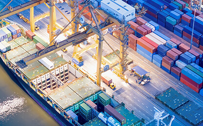 Aerial view of a busy shipping port at night with cargo containers, cranes, and a docked cargo ship by the water, reminiscent of the bustling activity managed daily by Chicago lawyers and law offices.