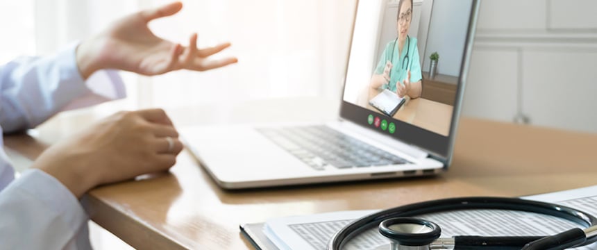 A person consults with a medical professional via video call on a laptop, with a stethoscope and documents on the desk in the foreground—ideal for litigation support in a corporate law office setting.