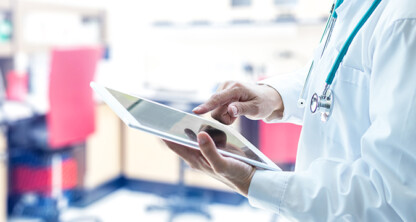 A medical professional in a white coat uses a tablet in a clinical setting, providing expertise that can aid law offices with litigation support, surrounded by lab equipment and a stethoscope around the neck.