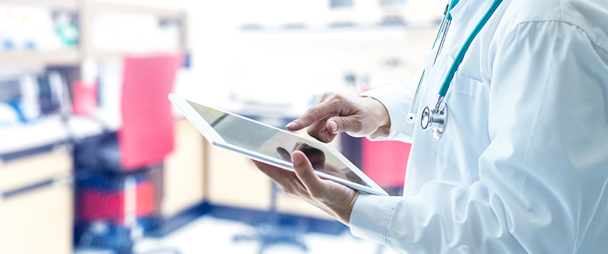 A medical professional in a white coat uses a tablet in a clinical setting, providing expertise that can aid law offices with litigation support, surrounded by lab equipment and a stethoscope around the neck.