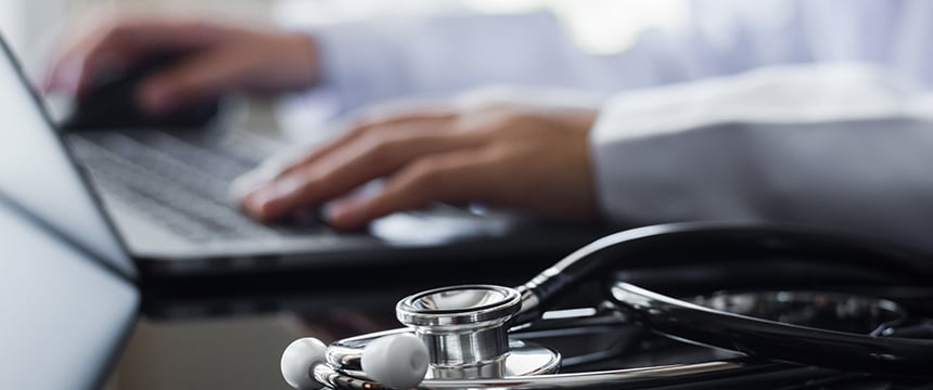 A person types on a laptop with a stethoscope resting on the desk in the foreground, highlighting the intersection of healthcare and intellectual property law.