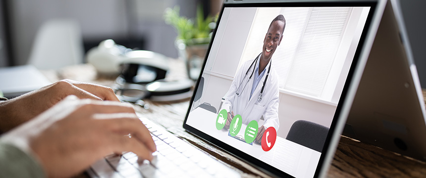 A person types on a laptop while participating in a video call with a doctor, similar to how chicago lawyers connect with clients remotely from a corporate law office.