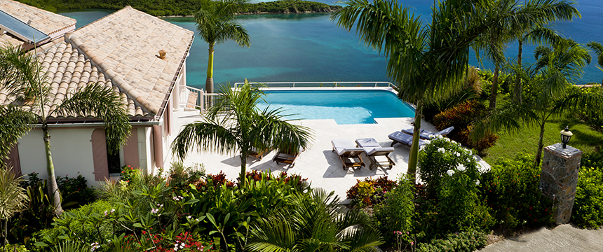 A villa with a tiled roof overlooks a pool, palm trees, and tropical landscaping, offering tranquil views—perfect for a corporate law office retreat or inspiration for those specializing in intellectual property law.