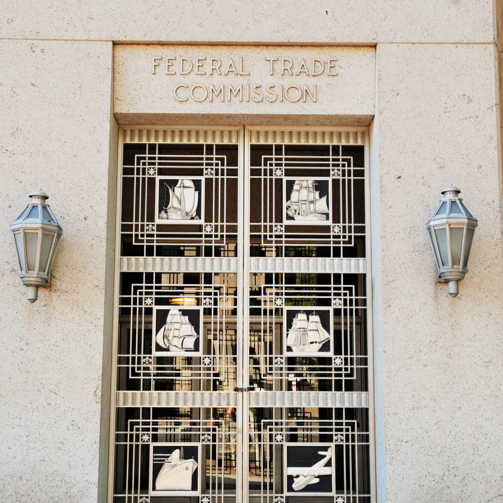 Entrance doors of the Federal Trade Commission building, featuring decorative metalwork with ship and airplane designs, flanked by two wall-mounted lanterns—an inspiring sight for any corporate law office or chicago lawyers seeking justice.