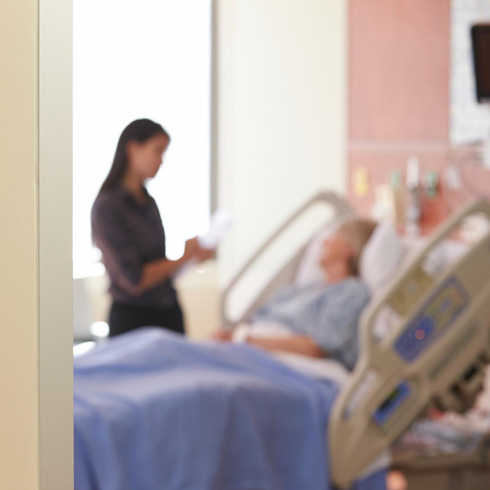 A patient lies in a hospital bed while another person, possibly a chicago lawyer or visitor, stands nearby holding papers. Both figures are out of focus.