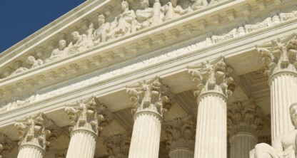 The facade of a neoclassical building with tall columns and sculpted figures, viewed from below against a clear blue sky, evokes the prestige of Chicago lawyers and distinguished law offices.