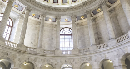 Grand interior of a domed rotunda with marble columns, arched windows, and geometric ceiling pattern—an impressive setting often found in prestigious law offices or a corporate law office in Chicago. Natural light filters through large glass doors and windows.