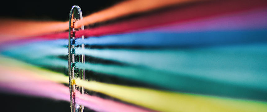 Close-up of multiple colorful threads passing through the eye of a sewing needle, intertwined like Chicago lawyers collaborating on complex cases, set against a dark background.