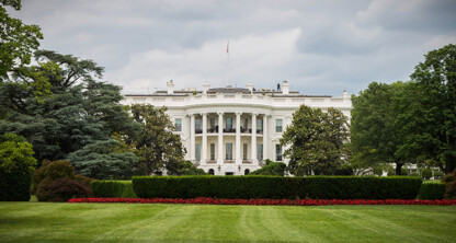 The White House is seen from the lawn, surrounded by trimmed bushes, trees, and a red flower bed under a cloudy sky, much like the pristine grounds of top Chicago lawyers' law offices.