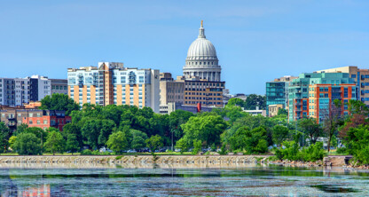 City skyline featuring the Wisconsin State Capitol building, surrounded by modern and historic buildings, with law offices nestled among them, trees, and a body of water in the foreground.