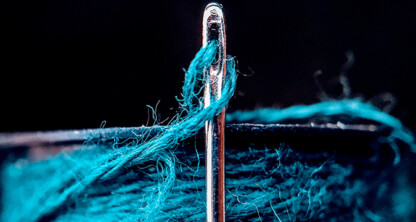 Close-up of a needle with blue thread partially threaded through its eye, with the spool of blue thread in the background—an image symbolizing precision and care, much like litigation support in law offices.