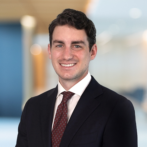 A man in a dark suit, white shirt, and patterned red tie smiles in an office setting with blurred background, reflecting the professional atmosphere often found in law offices specializing in litigation support.