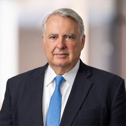 A middle-aged man in a dark suit, white shirt, and blue tie is smiling in an office setting with a blurred background, reflecting the professionalism of Chicago lawyers specializing in intellectual property law.