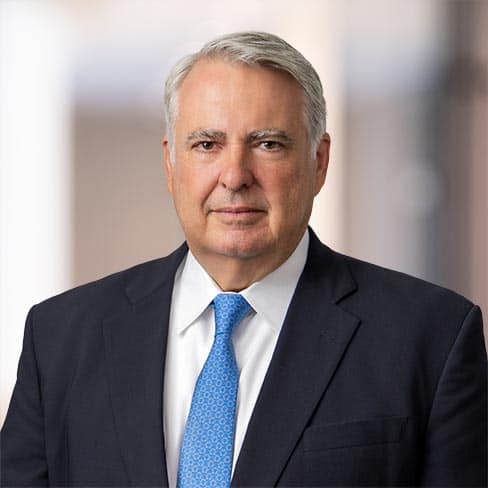 A middle-aged man in a dark suit, white shirt, and blue tie is smiling in an office setting with a blurred background, reflecting the professionalism of Chicago lawyers specializing in intellectual property law.