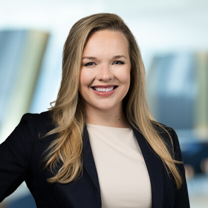 A woman with long blonde hair, wearing a dark blazer and light top, smiles at the camera against a blurred office background, embodying the professionalism of leading lawyers in Chicago.