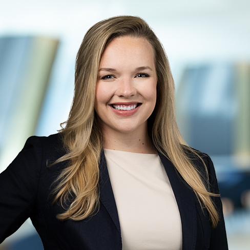 A woman with long blonde hair, wearing a dark blazer and light top, smiles at the camera against a blurred office background, embodying the professionalism of leading lawyers in Chicago.
