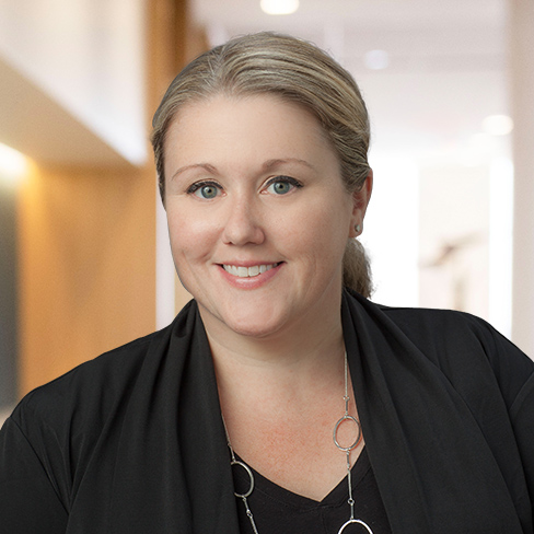 A woman with blonde hair pulled back, wearing a black top and jacket, smiles at the camera in a brightly lit indoor setting—reflecting the professionalism of lawyers in Chicago specializing in intellectual property law.