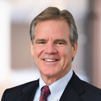 A middle-aged man in a dark suit, light blue shirt, and patterned tie smiles at the camera against a blurred indoor background, reflecting his experience in litigation support for law offices.