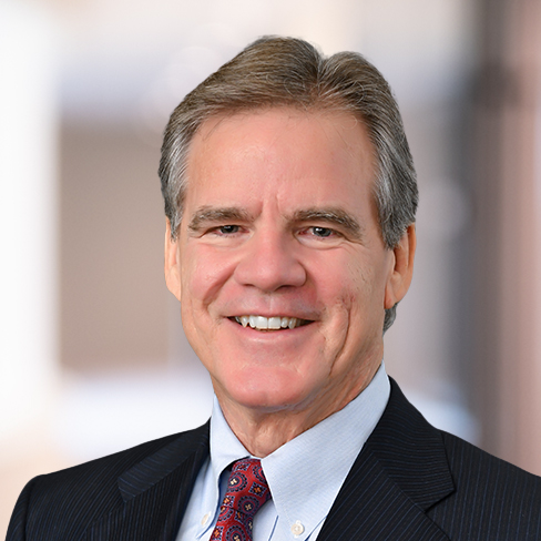A middle-aged man in a dark suit, light blue shirt, and patterned tie smiles at the camera against a blurred indoor background, reflecting his experience in litigation support for law offices.