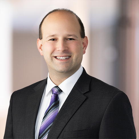 A man in a dark suit, white shirt, and purple striped tie smiles at the camera against a blurred office background, reflecting the professionalism found in top Chicago lawyers and law offices.