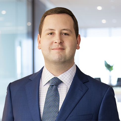 A man in a blue suit and patterned tie stands in a modern law office with glass walls and a blurred background, reflecting a professional environment for litigation support.