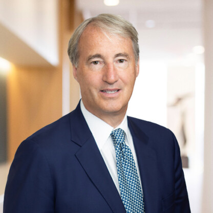 A middle-aged man with gray hair, wearing a dark blue suit, white shirt, and patterned blue tie, stands in a bright, modern law office hallway—an ideal setting for Chicago lawyers offering litigation support.