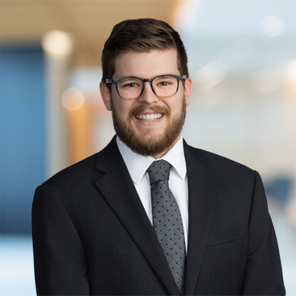 A man with glasses and a beard wears a dark suit, white shirt, and patterned tie, standing against a blurred indoor background in a corporate law office, representing litigation support for lawyers in Chicago.