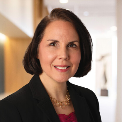 A woman with short dark hair, wearing a black blazer, gold necklace, and red top, smiles in a well-lit law offices setting with a blurred background.