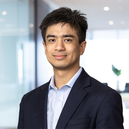 A man in a dark blazer and light blue shirt stands in a modern office with glass walls, embodying the professionalism of lawyers in Chicago dedicated to litigation support. Blurred background elements complete the contemporary setting.