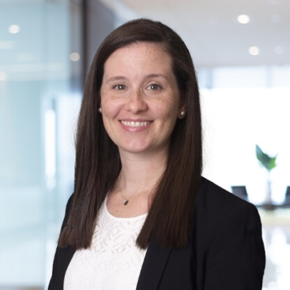A woman with long brown hair, wearing a black blazer and white top, smiles at the camera in a modern office setting, representing leading chicago lawyers specializing in intellectual property law.