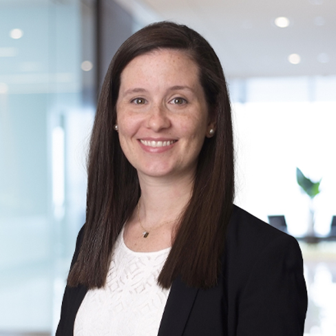 A woman with long brown hair, wearing a black blazer and white top, smiles at the camera in a modern office setting, representing leading chicago lawyers specializing in intellectual property law.