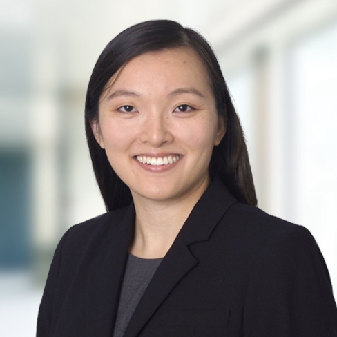 A woman with straight dark hair, wearing a black blazer and grey top, smiles at the camera against a blurred office background—an experienced professional among leading lawyers in Chicago.
