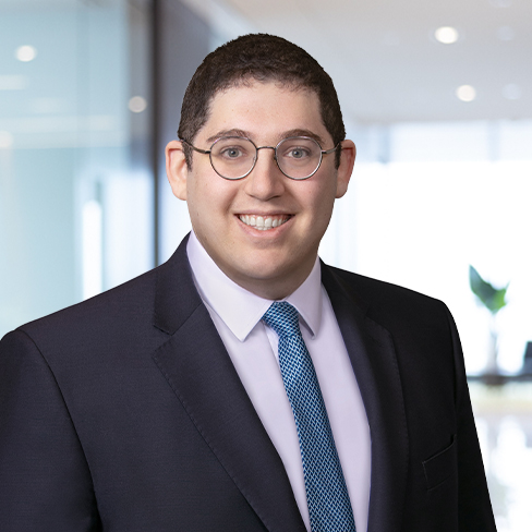 A man wearing glasses, a dark suit, a white shirt, and a blue patterned tie stands in a modern, well-lit law office, representing skilled lawyers in Chicago.