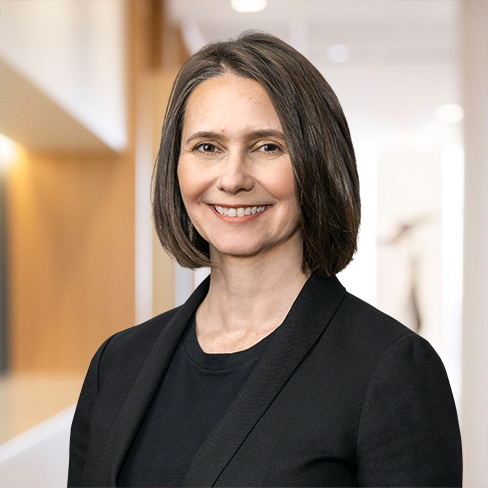 A woman with straight, shoulder-length brown hair wearing a black blazer and black top, standing indoors and smiling at the camera—representing chicago lawyers who specialize in intellectual property law.